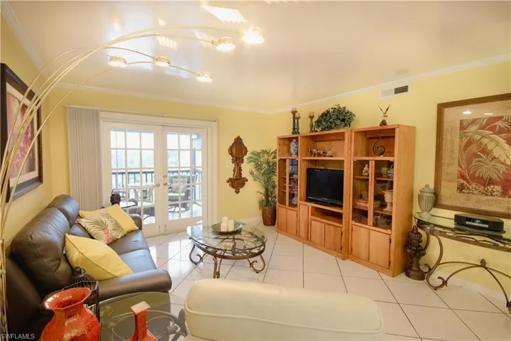 Living room with ornamental molding, light tile patterned flooring, and french doors