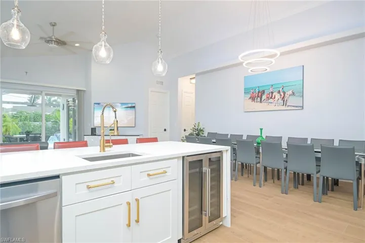 Kitchen with white cabinetry, wine cooler, stainless steel dishwasher, hanging light fixtures, and sink