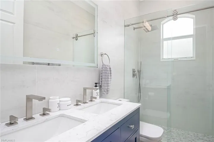 Bathroom featuring double vanity, walk in shower, and toilet