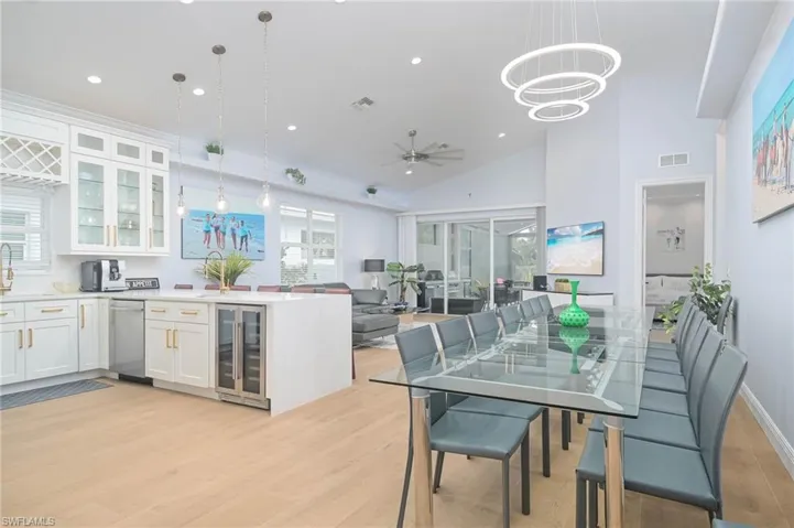 Dining area with plenty of seating , open floorplan, new flooring, ceiling fan with notable chandelier, new kitchen with wine cooler, and a healthy amount of sunlight