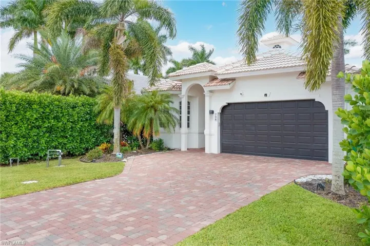 Contemporary home featuring a 2-car garage, paved driveway, tile roof, and lush landscaping