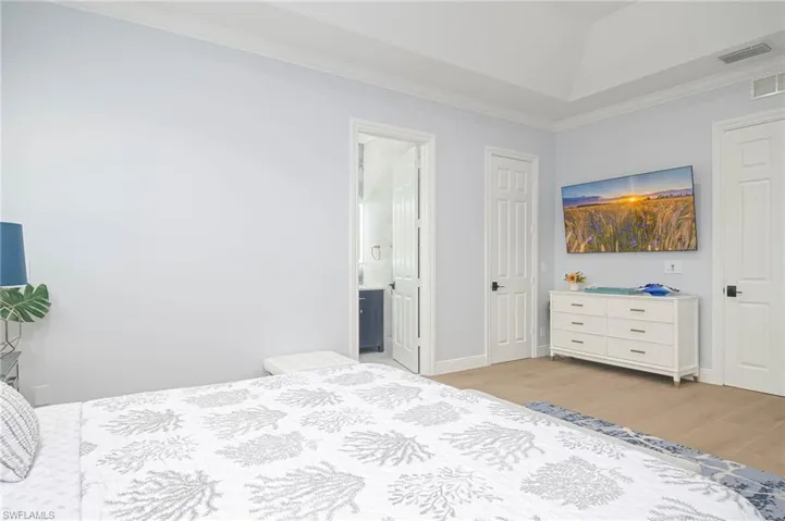 Primary Bedroom with ensuite bath, light hardwood / wood-style flooring, lofted ceiling, and ornamental molding