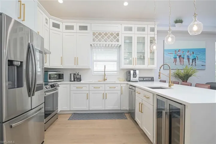 Kitchen with white cabinetry, light wood-type flooring, wine cooler, hanging light fixtures, and appliances with stainless steel finishes