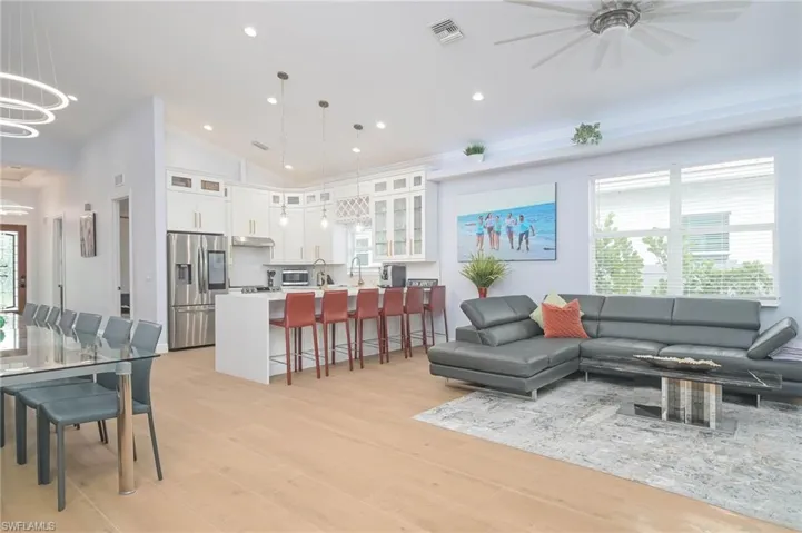 Living room with light hardwood / wood-style floors, a healthy amount of sunlight, ceiling fan with notable chandelier, and vaulted ceiling