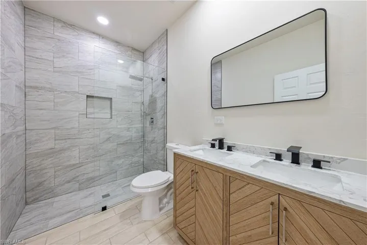Primary bath with double vanity, a tile shower, and recessed lighting