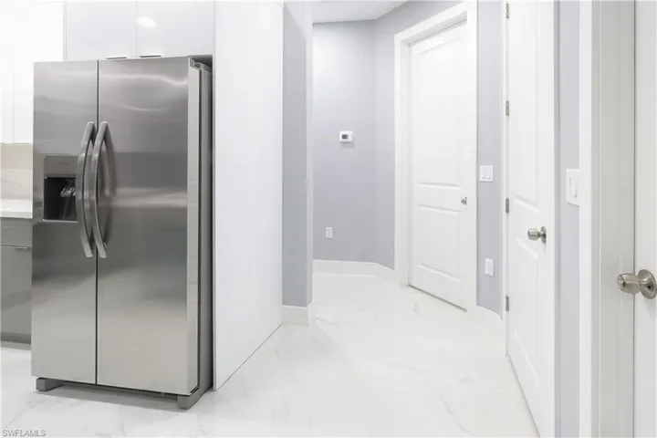 Kitchen featuring stainless steel refrigerator with ice dispenser, light marble finish flooring, light countertops, and modern cabinets