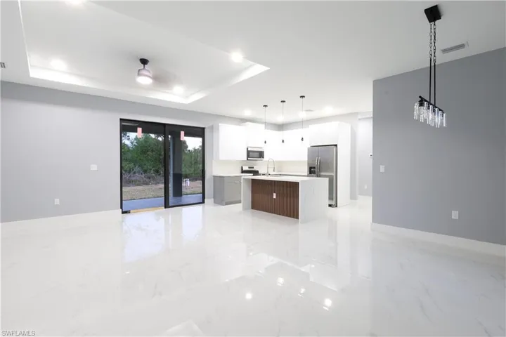 Kitchen with light countertops, a kitchen island with sink, open floor plan, appliances with stainless steel finishes, and a raised ceiling