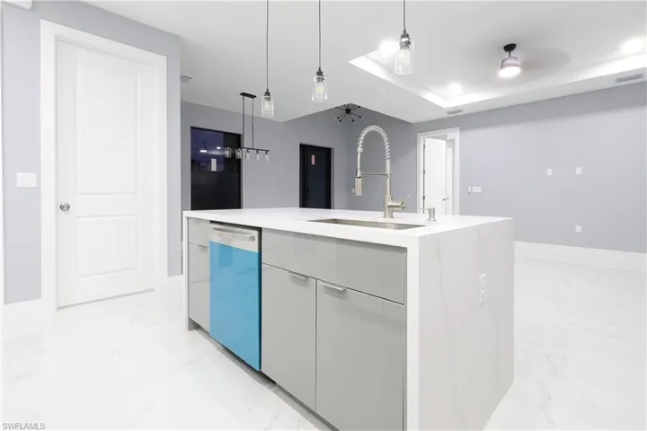 Kitchen with modern cabinets, light marble finish floors, a center island with sink, dishwasher, and decorative light fixtures