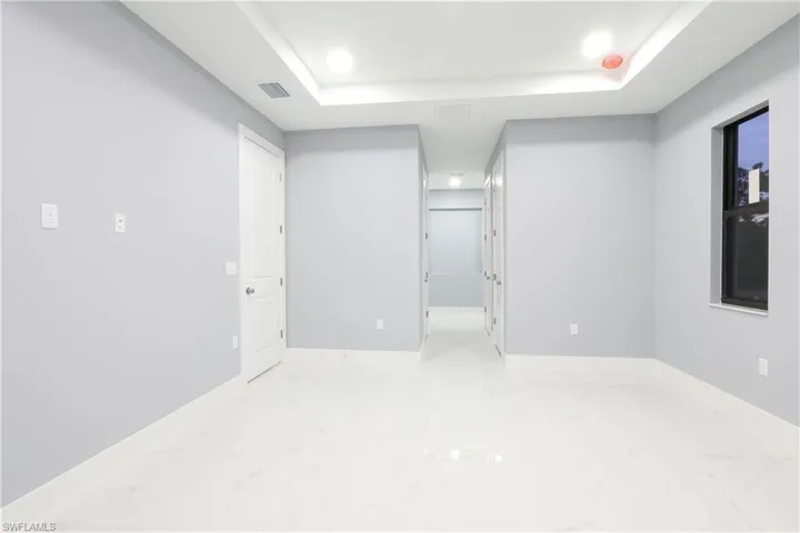Unfurnished bedroom featuring a tray ceiling, light marble finish flooring, and recessed lighting