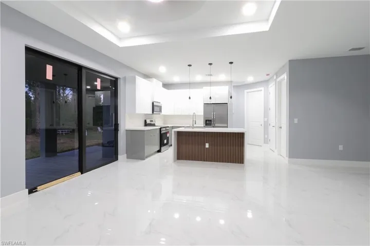 Kitchen with stainless steel appliances, light countertops, pendant lighting, an island with sink, and light marble finish flooring