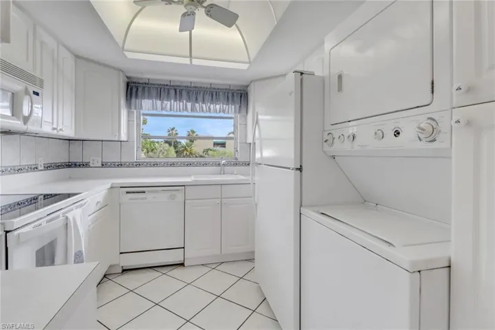 Kitchen featuring stacked washer / drying machine, white appliances, ceiling fan, white cabinets, and light countertops