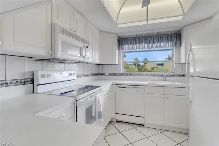 Kitchen featuring white appliances, white cabinetry, light countertops, decorative backsplash, and light tile patterned floors