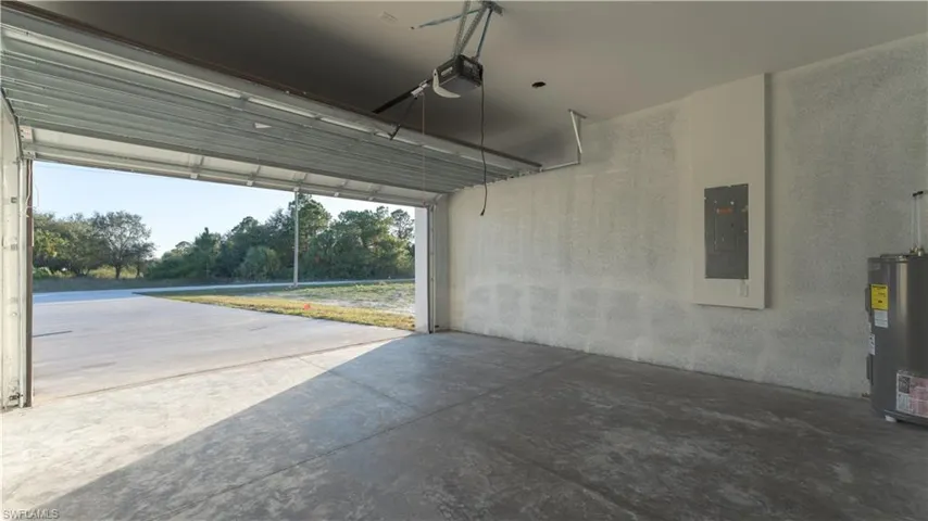 Garage with electric water heater, electric panel, and a garage door opener