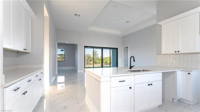 Kitchen featuring kitchen peninsula, tasteful backsplash, a tray ceiling, sink, and white cabinets