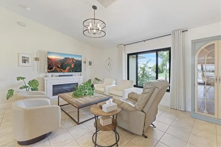 Living area featuring vaulted ceiling, light tile patterned floors, a chandelier, and a glass covered fireplace