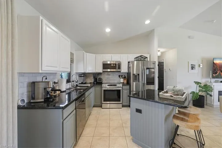 Kitchen featuring stainless steel appliances, vaulted ceiling, decorative backsplash, a breakfast bar, and dark stone countertops