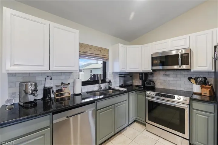 Kitchen with stainless steel appliances, vaulted ceiling, tasteful backsplash, and white cabinets