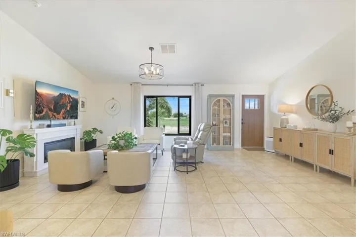 Living room featuring vaulted ceiling, light tile patterned floors, a chandelier, and a glass covered fireplace