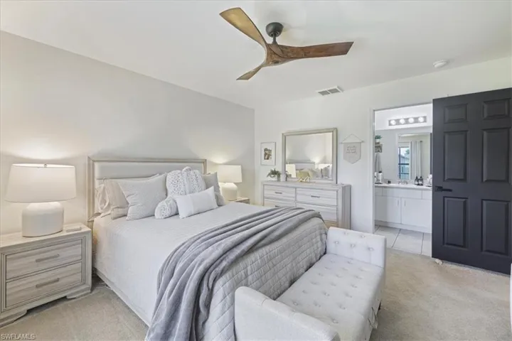 Bedroom with light colored carpet, connected bathroom, and a ceiling fan