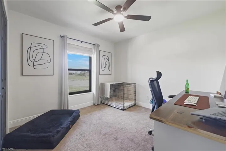 Carpeted home office with a ceiling fan and baseboards