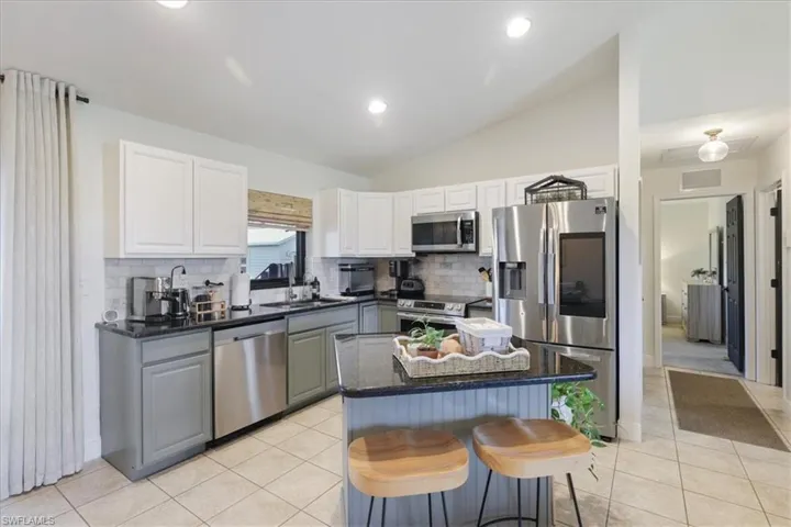 Kitchen featuring appliances with stainless steel finishes, backsplash, light tile patterned floors, vaulted ceiling, and white cabinets