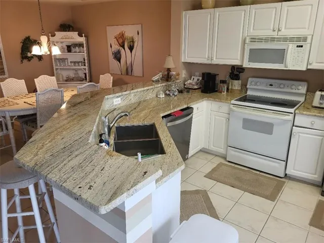 Kitchen with a breakfast bar area, white appliances, a peninsula, white cabinets, and light tile patterned flooring