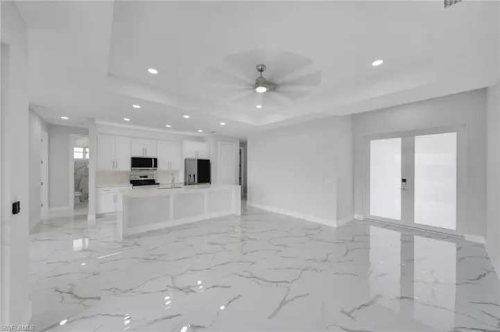 Unfurnished living room with a tray ceiling, recessed lighting, french doors, ceiling fan, and baseboards