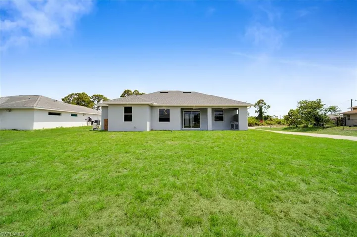 Rear view of house with a lawn, stucco siding, and roof with shingles