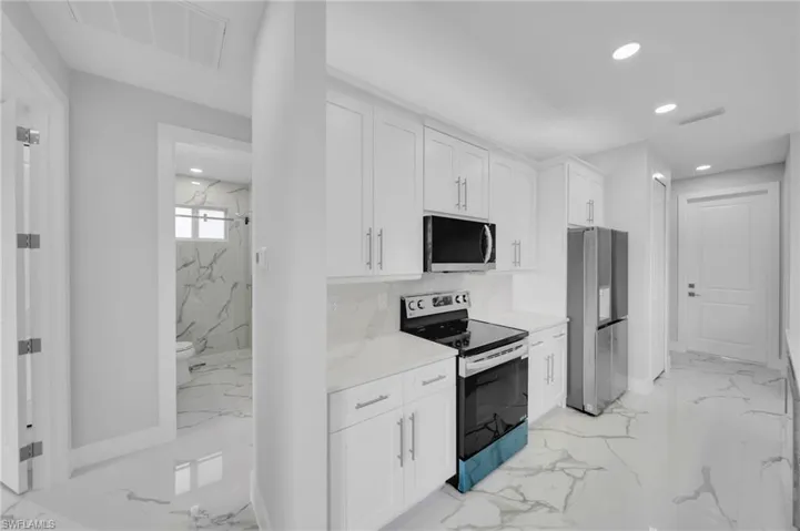 Kitchen featuring appliances with stainless steel finishes, light marble finish flooring, recessed lighting, white cabinetry, and light countertops