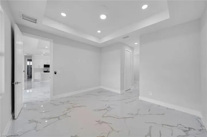 Empty room featuring recessed lighting, a tray ceiling, light marble finish flooring, and baseboards
