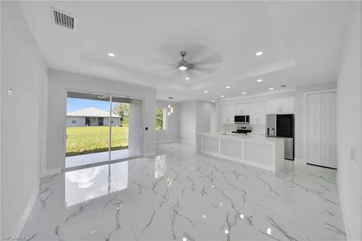 Unfurnished living room with a tray ceiling, recessed lighting, a sink, light marble finish floors, and baseboards