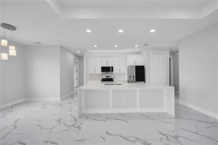 Kitchen with appliances with stainless steel finishes, recessed lighting, baseboards, white cabinetry, and a large island