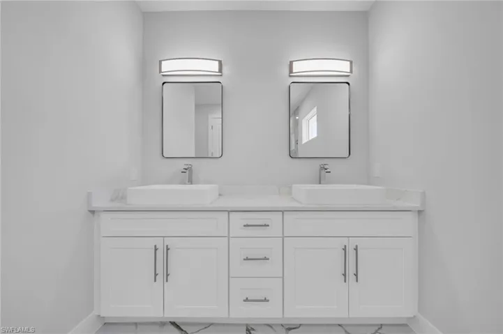 Full bath featuring marble look tile flooring, baseboards, and double vanity