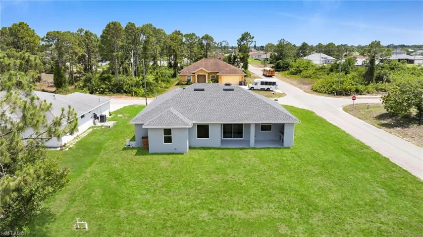 Back of house featuring a shingled roof, a lawn, a residential view, and stucco siding