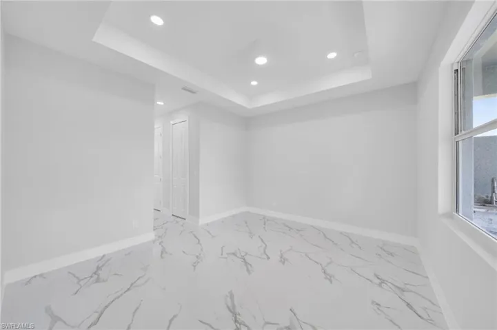 Spare room featuring recessed lighting, a tray ceiling, marble finish floors, and baseboards