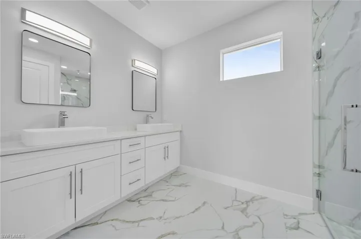 Bathroom featuring a marble finish shower, double vanity, baseboards, and marble look tiles