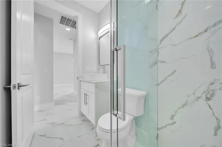 Bathroom with toilet, vanity, marble look tiles, and baseboards