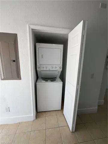 Washroom featuring electric panel, stacked washer / dryer, light tile patterned flooring, and a textured ceiling