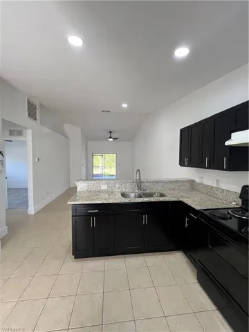 Kitchen with dark cabinets, range, light stone countertops, a ceiling fan, and recessed lighting