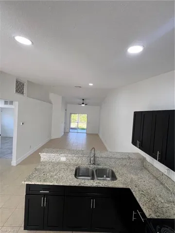 Kitchen featuring dark cabinets, light tile patterned floors, a ceiling fan, open floor plan, and light stone counters