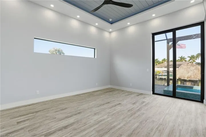 Spare room featuring light wood finished floors, ceiling fan, plenty of natural light, a raised ceiling, and recessed lighting