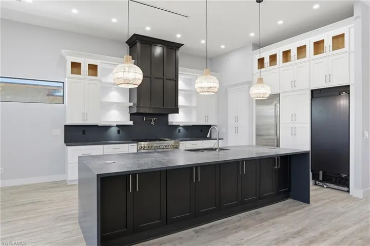 Kitchen featuring dark cabinets, glass insert cabinets, a large island with sink, white cabinetry, and light wood-type flooring