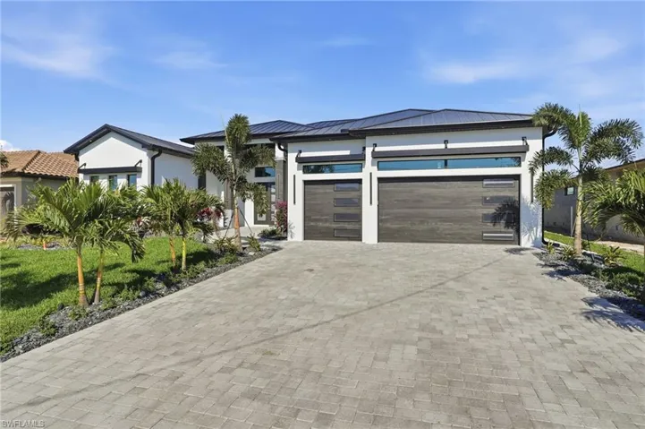 View of front of property with decorative driveway, an attached garage, a metal roof, and stucco siding