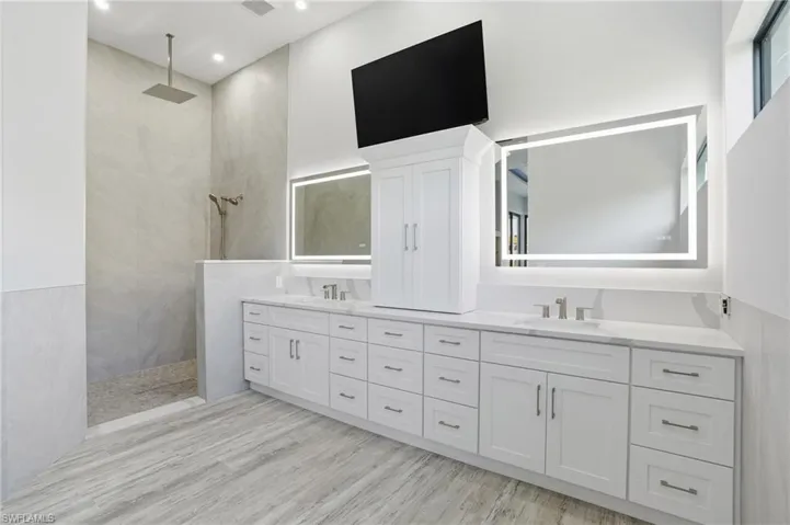 Full bath with double vanity, walk in shower, and light wood-style floors