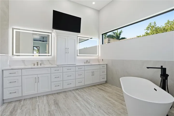 Bathroom with double vanity, a freestanding tub, light wood-style flooring, and tile walls