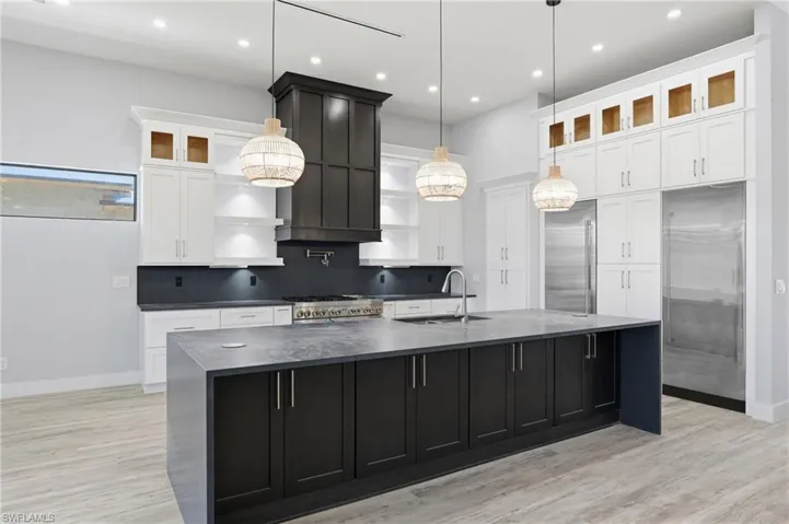Kitchen with dark cabinetry, glass insert cabinets, white cabinets, a large island, and light wood-type flooring