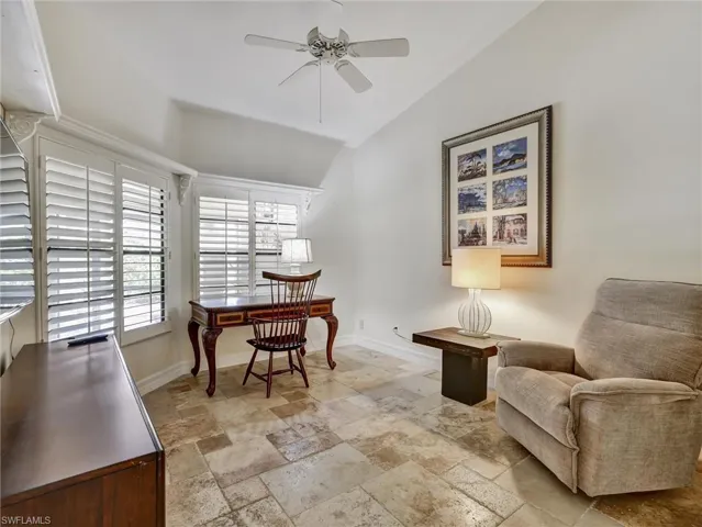 Den with stone tile floors, an office area, a ceiling fan, and vaulted ceiling