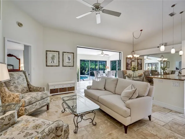 Living room featuring lofted ceiling, a ceiling fan, stone tile floors, and a chandelier