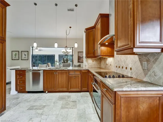 Kitchen with brown cabinets, light stone countertops, and backsplash
