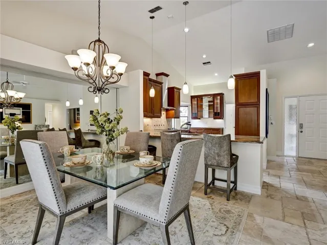 Dining room with vaulted ceiling, stone tile floors, a chandelier, and recessed lighting